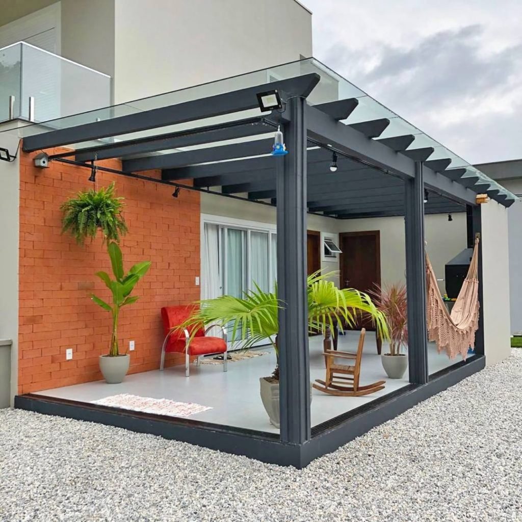 Pergolado de concreto como extensão da casa com cobertura de vidro para maior proteção e aconchego